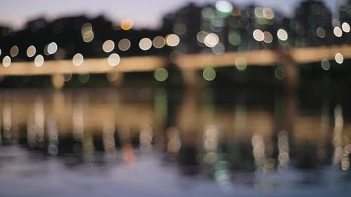 Blurry bokeh lights of a city reflect off a glasslike river.