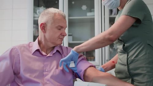 Nurse in Uniform Places Tourniquet to Identify Viable and Accessible Vein on Old Man Arm