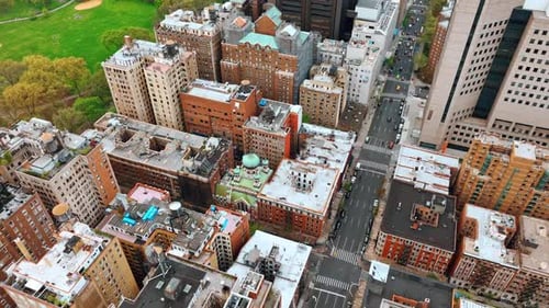 Flying over the residential area and avenue in New York. Green park near the buildings at backdrop.