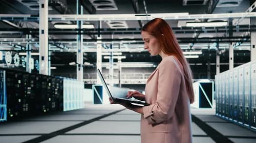 Woman in Server Farm Using Laptop to Improve Electronics Optimizations