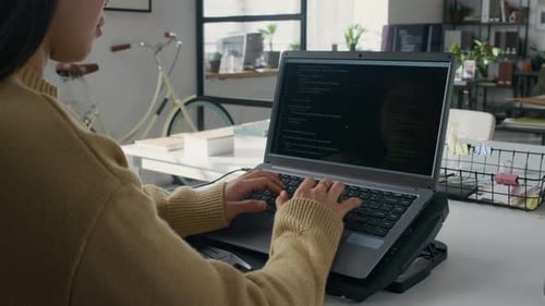 Female Developer Coding on Laptop Placed on Cooling Stand in Modern Office