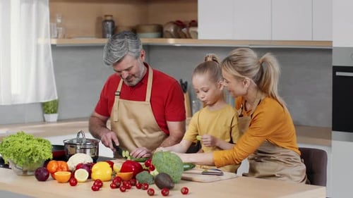 Happy Middle Aged Parents Preparing Dinner Together with Little Daughter Girl Feeding Her Mother