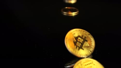 Nahaufnahme: Die physische Goldmünze von Bitcoin fällt auf einen schwarzen Glastisch. Leerzeichen kopieren. Zeitlupe.