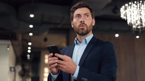 Focused Gentleman Standing in Hall and Texting Messages on Modern Smartphone