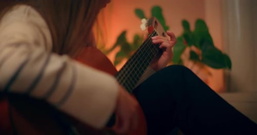 Woman Playing Guitar at Home in Soft Light