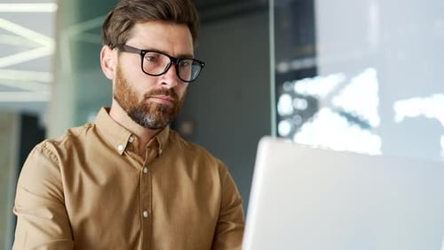 Serious thoughtful manager works on a laptop sitting at workplace in a business office.