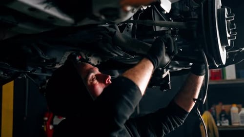 an Auto Mechanic at a Service Station Unscrews the Bolts Under the Body with a Wrench