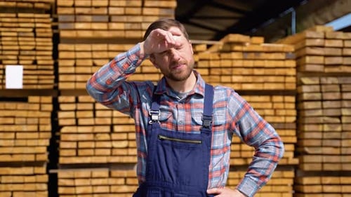 Tired Young Male Worker in Timber Lumber Warehouse