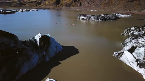 Aerial panoramic view of people kayaking next to Sólheimajökull glacier, in Iceland, on a sunny day