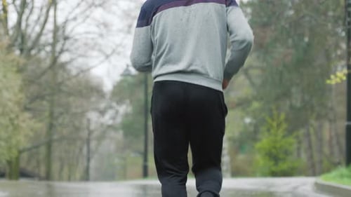 Hooded Man Exercising in City Park in Rain
