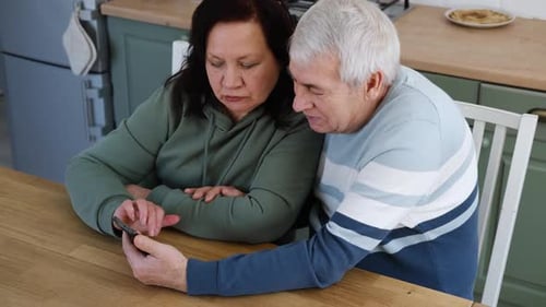 Senior Couple Using Smartphone Together in Kitchen