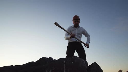 Kaukasischer Mann mit Bart steht und schlägt mit einer Spitzhacke auf die Steine, Funken und Steinstücke fliegen