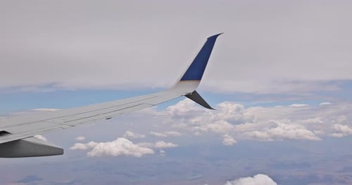 Durch ein Fenster beobachten wir einen Flugzeugflügel, der über Wolken fliegt, vor dem Hintergrund von Fluffy