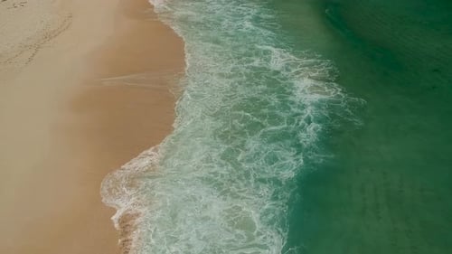 Waves breaking onto a beach as view from above, shot with a drone at4K