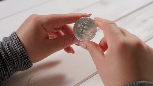 Young Woman Trader Investor Holds Silver Bitcoin on a Light Wooden Background