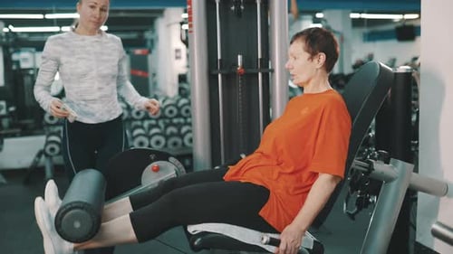 Personal Trainer instruindo mulher sênior sobre máquina de extensão de pernas