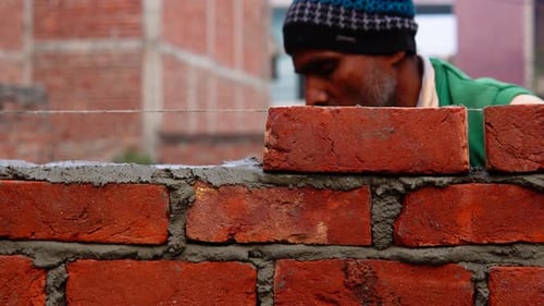 Skilled laborer places bricks in rows over cement to construct a wall