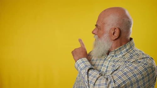 Senior Man Points to the Side on Yellow Background