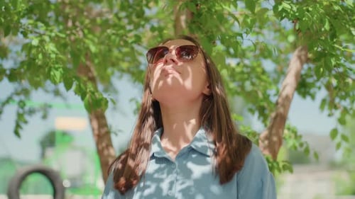 Woman with Sunglasses Standing Under Tree in Park
