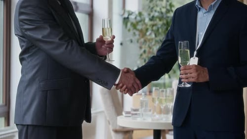 Businessmen handshake with champagne glasses in a bright location