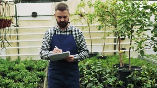 Man taking notes in plant nursery greenhouse