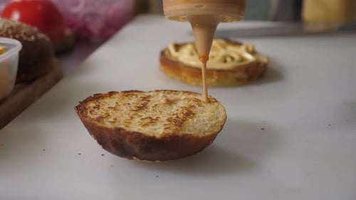 The Chef Puts White Sauce on Half of a Grilled Burger Bun