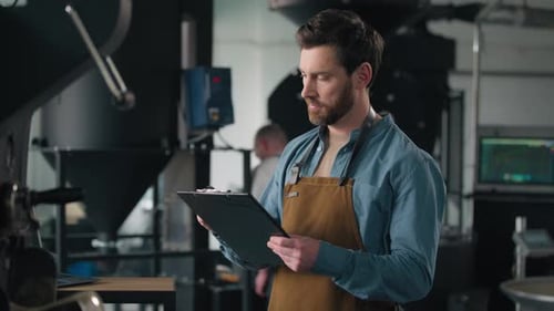Man Inspecting Coffee Roasting Machinery at Workplace