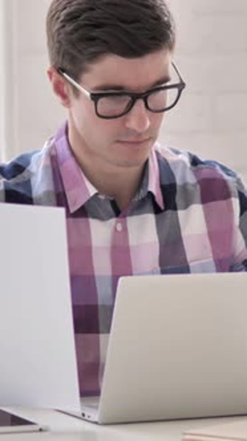 Man with Glasses Works with Laptop and Documents