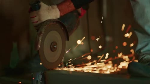Metal worker using grinder with sparks in factory