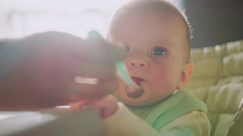 Infant eating food in a high chair close up