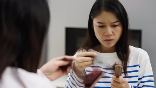 stressed woman suffering hair loss problem with her hairbrush in mirror at home