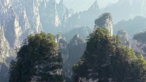 Drone flying above misty peaks and green forest-covered pillars in Zhangjiajie site, dreamy