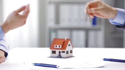 Real estate agent handing over house keys to a happy new homeowner woman in office