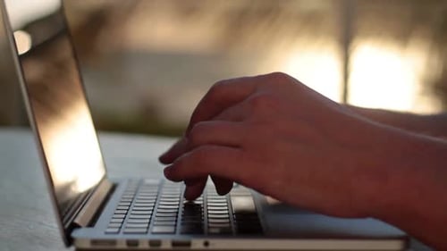Man Typing on a Laptop at Sunset Beach