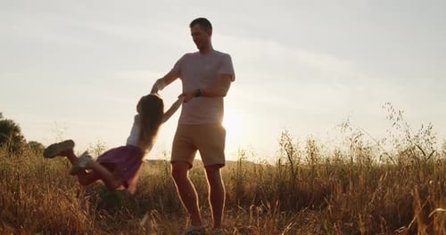 Happy Father Spinning His Daughter Holding Hands in a Golden Field at Sunset