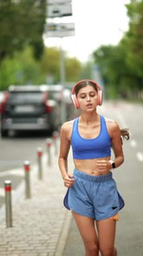Engaged in Her Morning Jog a Pretty Girl in Athletic Attire and Headphones Runs Through the City