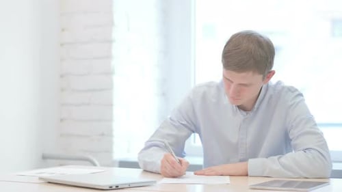 Young Businessman Writing while Sitting in Office
