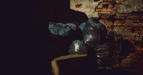Discarded Waste Bags Pile Near Weathered Brick Wall at Dusk
