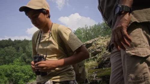 Polyethnic Boy and Dad with Backpacks Trekking down Rocky Hills in Summer
