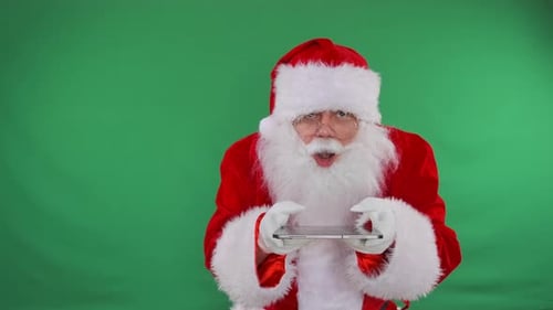 Santa scrolls screen tablet shocked by big discounts for New year and Christmas, green background.