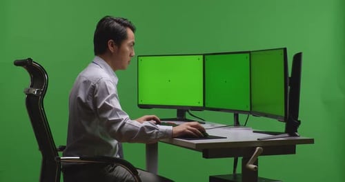 Asian Man Working With Mock Up Multiple Computer Monitor In Green Screen Studio
