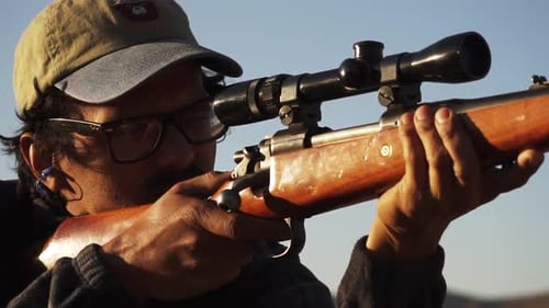 Man Aims Rifle with Scope in Desert Setting