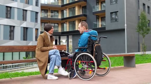 Woman Talking to Man in Wheelchair on Bench