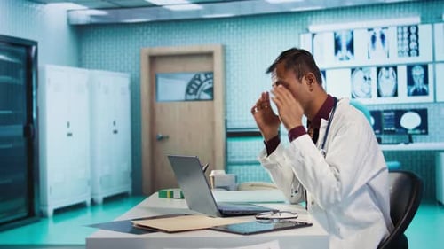 Overworked Doctor Sitting at Desk in Hospital Office