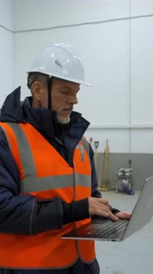 Vertical of Engineer Examines Premise of Warehouse Holding Laptop