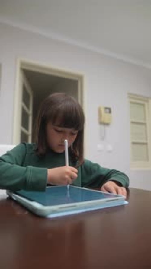 A Young Child Deeply Engaged with a Tablet and Stylus While Sitting in a Brightly Lit Room