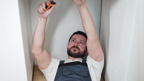 Starker Mechaniker, der auf dem Boden liegt und beim Schielen das Ventil mit einem Schraubenschlüssel festzieht