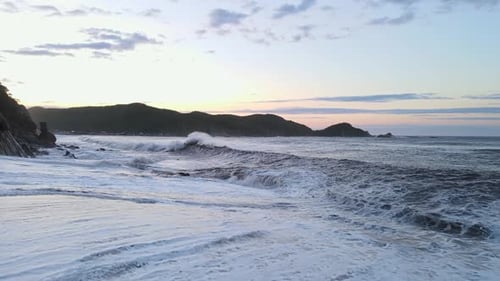 Low Flight of a Drone Over a Large Storm Wave Rolling Onto a Rocky Shore at Dawn