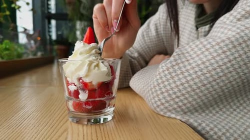 A Woman is Savoring a Fresh Strawberry Cream Dessert at a Cozy Cafe Enjoying a Delicious Treat in a
