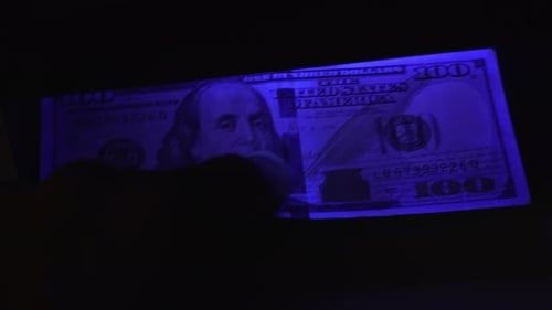 Hand Holding One Hundred Dollar Bill Under Blue Light
